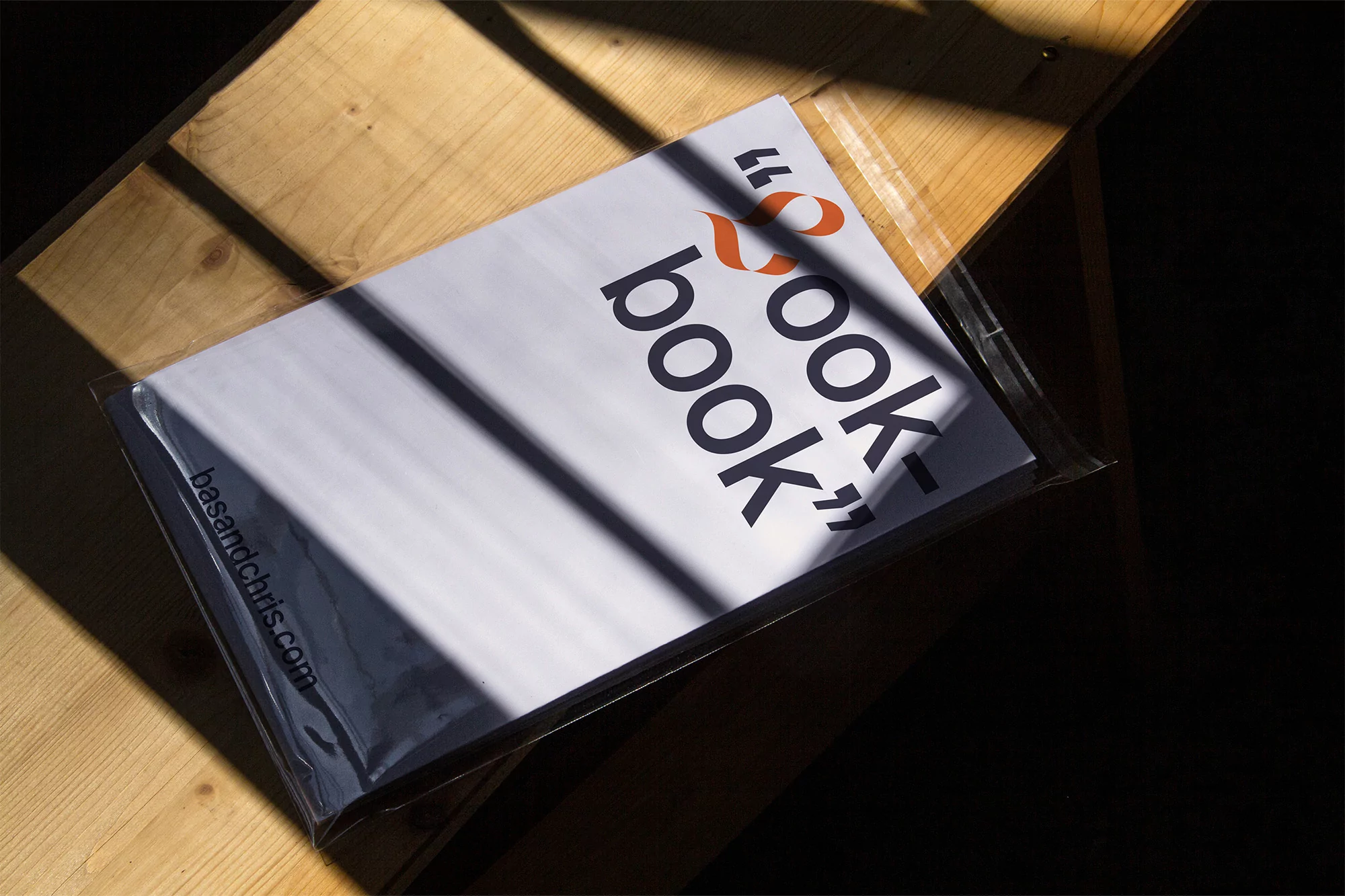 Studio shot of a cookbook on a wooden table featuring contrasting shadows and light, with bold typography and a modern design.