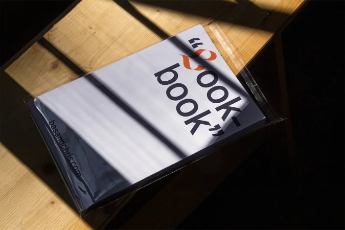 Studio shot of a cookbook on a wooden table featuring contrasting shadows and light, with bold typography and a modern design.