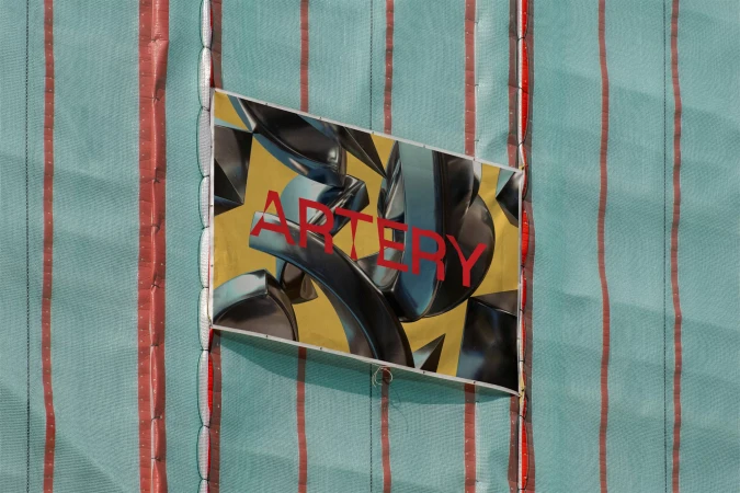 Abstract banner with the word 'Artery' in red, hanging on a green construction fence with red stripes, outdoor advertisement.