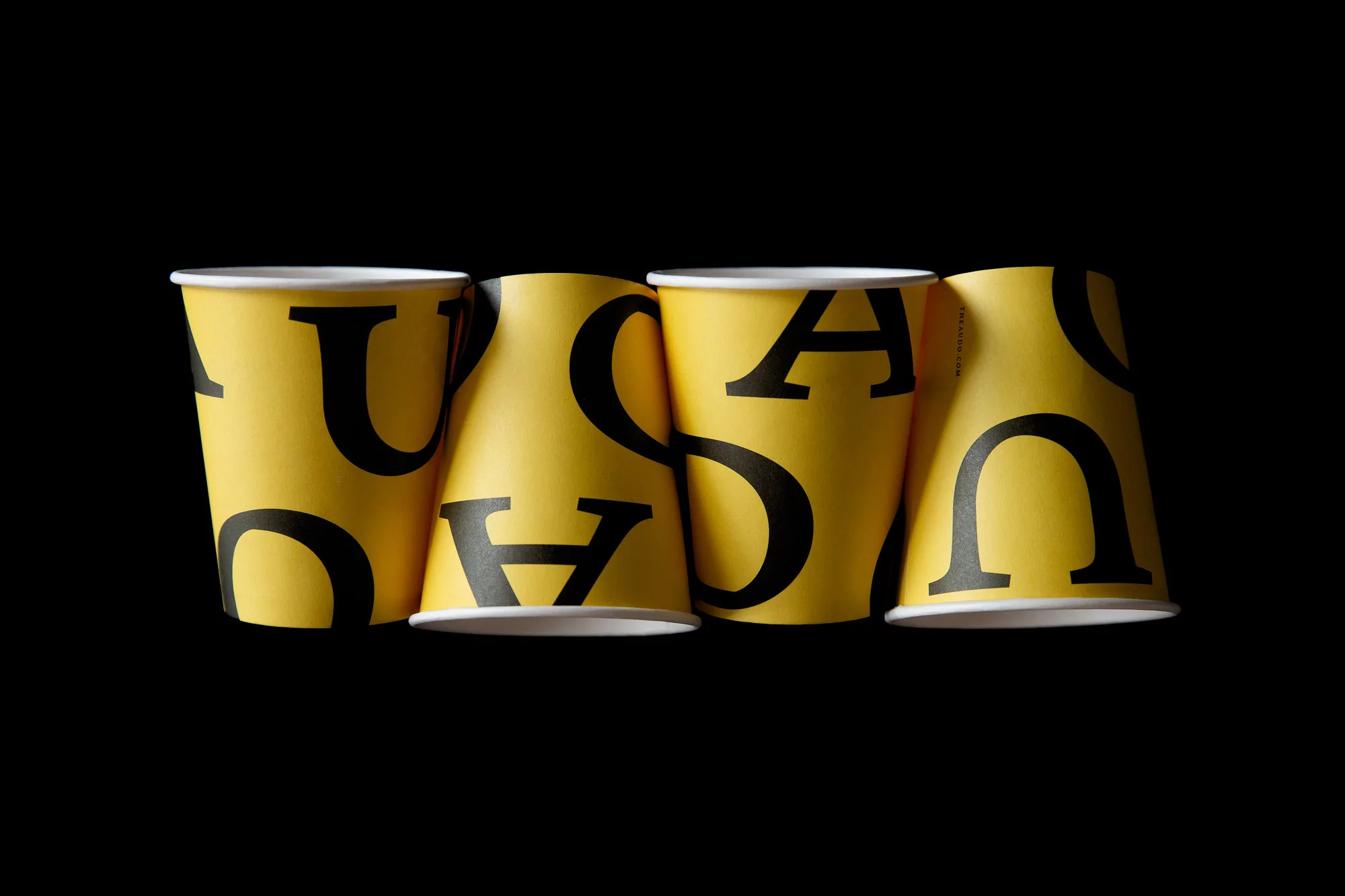 Row of yellow disposable cups with black uppercase letters in a studio setting against a black background.