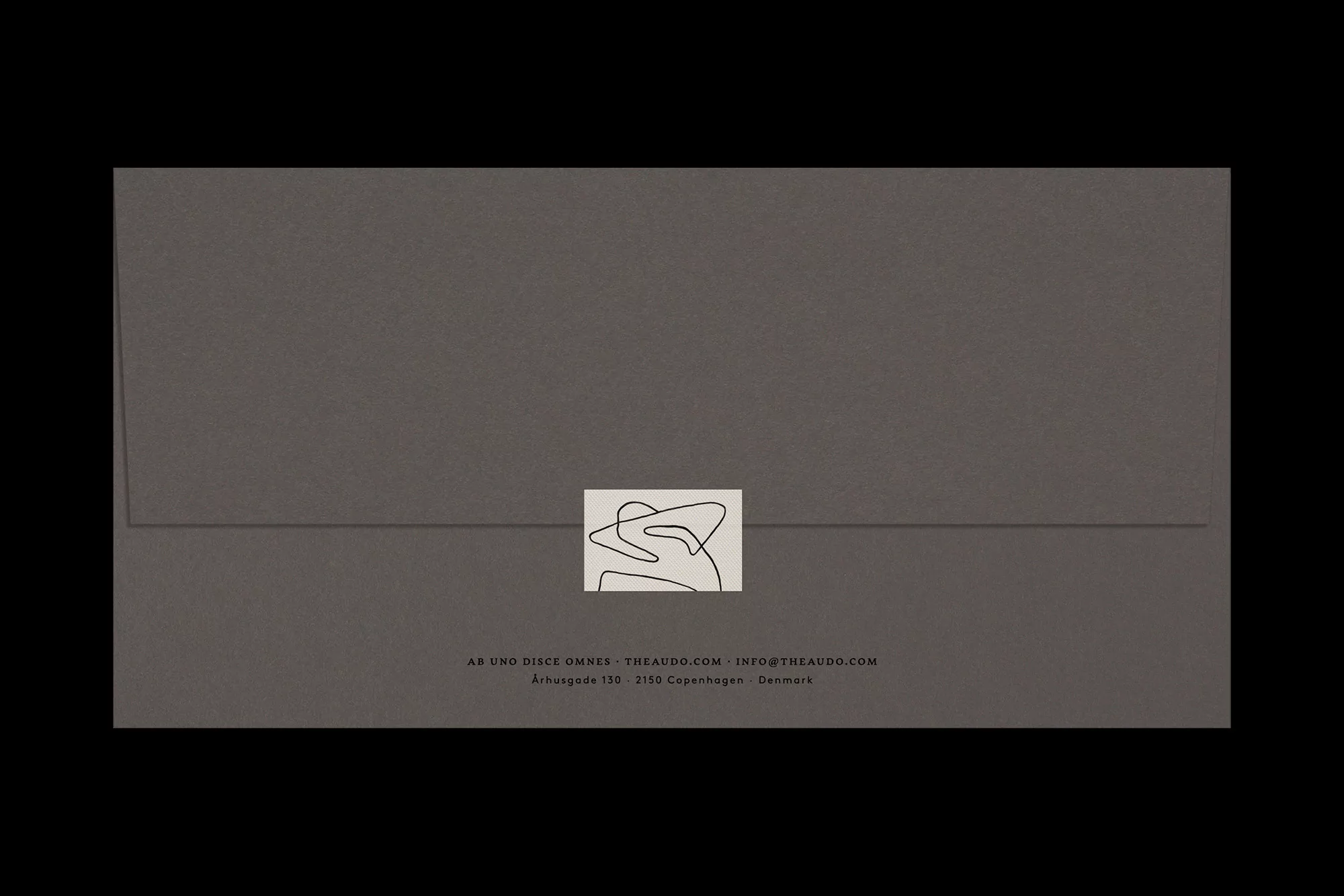 Minimalist studio shot of a sealed gray envelope with a logo and text against a black background. Clean design and simple visual.