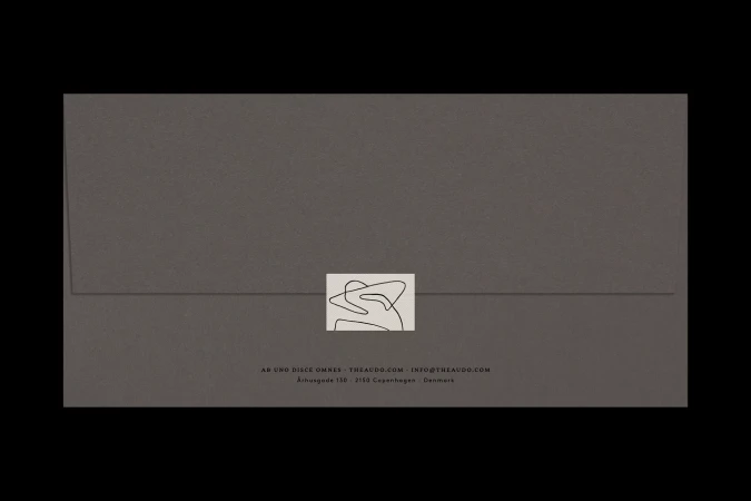 Minimalist studio shot of a sealed gray envelope with a logo and text against a black background. Clean design and simple visual.