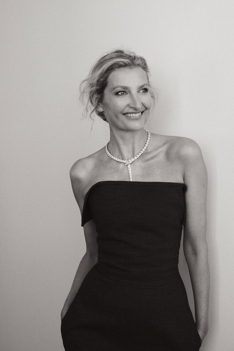Elegant black and white portrait of a woman in a strapless dress and diamond necklace, smiling softly against a neutral backdrop.