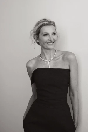 Elegant black and white portrait of a woman in a strapless dress and diamond necklace, smiling softly against a neutral backdrop.