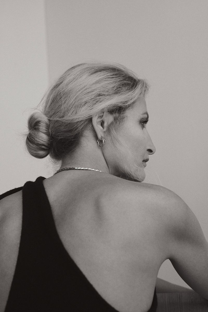 Black and white portrait of a fair-skinned woman with blonde hair styled in a bun, wearing a black dress and facing right.