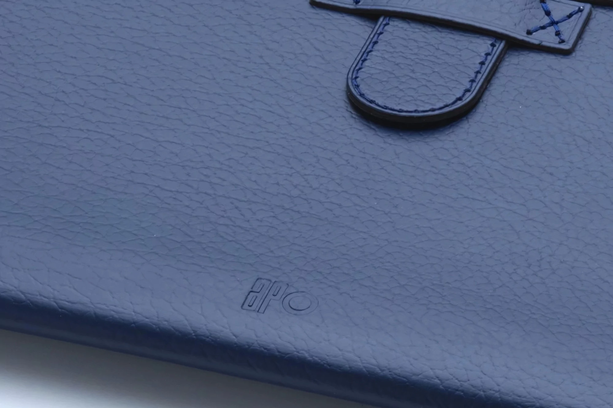 Close-up of a navy blue leather folio case with embossed logo and stitched closure, showcasing texture and detail.