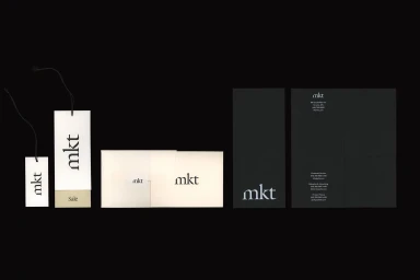 Mkt brand identity layout featuring white hang tags, off-white envelopes, and black stationery items on a dark background.
