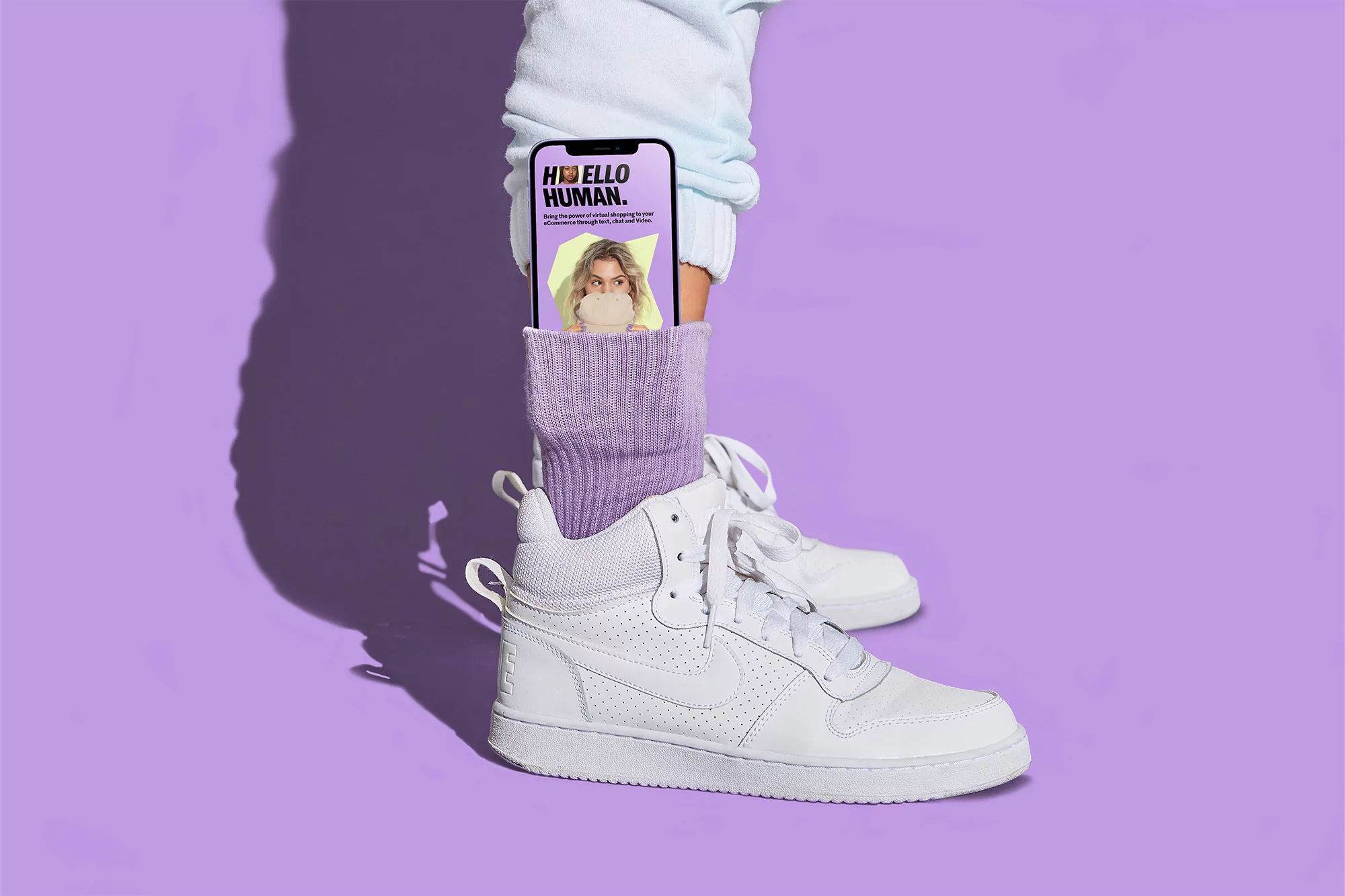 High-angle shot of a white sneaker with a purple sock holding a smartphone displaying a blonde woman blowing bubblegum.