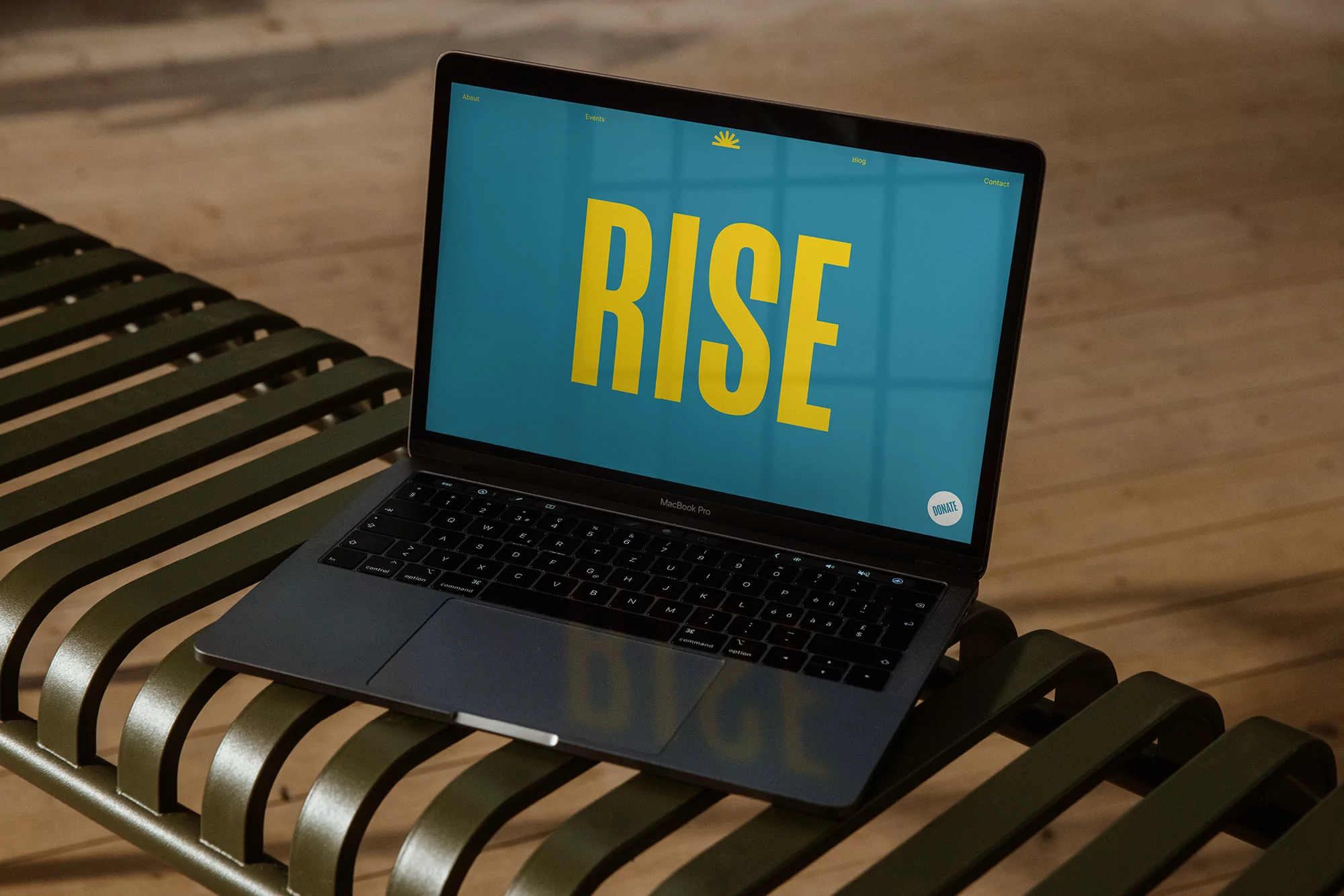 Laptop displays RISE text on a bench, creating a modern, tech-focused scene with natural light and a minimalist aesthetic.
