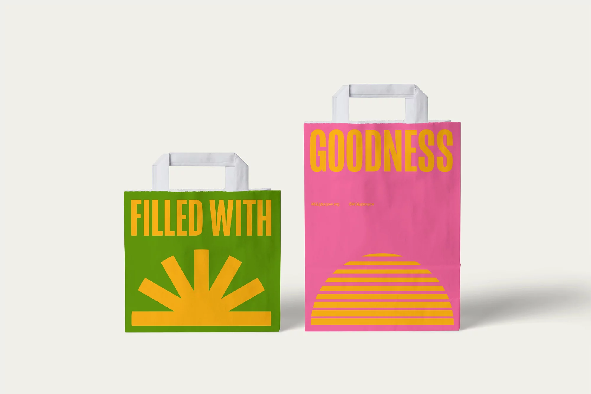 Two paper shopping bags, one green with 'Filled With' text and graphic, the other pink with 'Goodness' text and graphic.