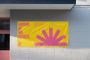 A yellow banner with pink typography mounted on a grey painted brick wall outdoors