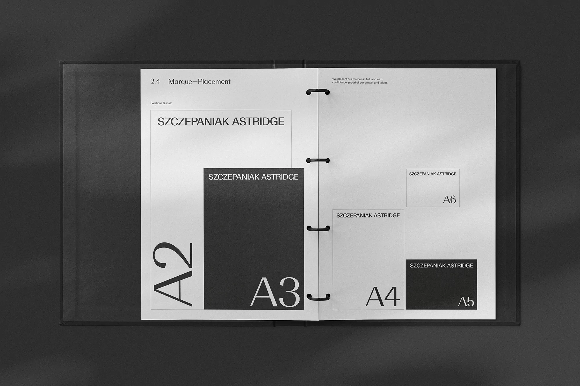 Open binder showcasing graphic design layouts with text 'Szczepaniak Astridge' alongside paper sizes A2, A3, A4, A5, and A6 on white paper.