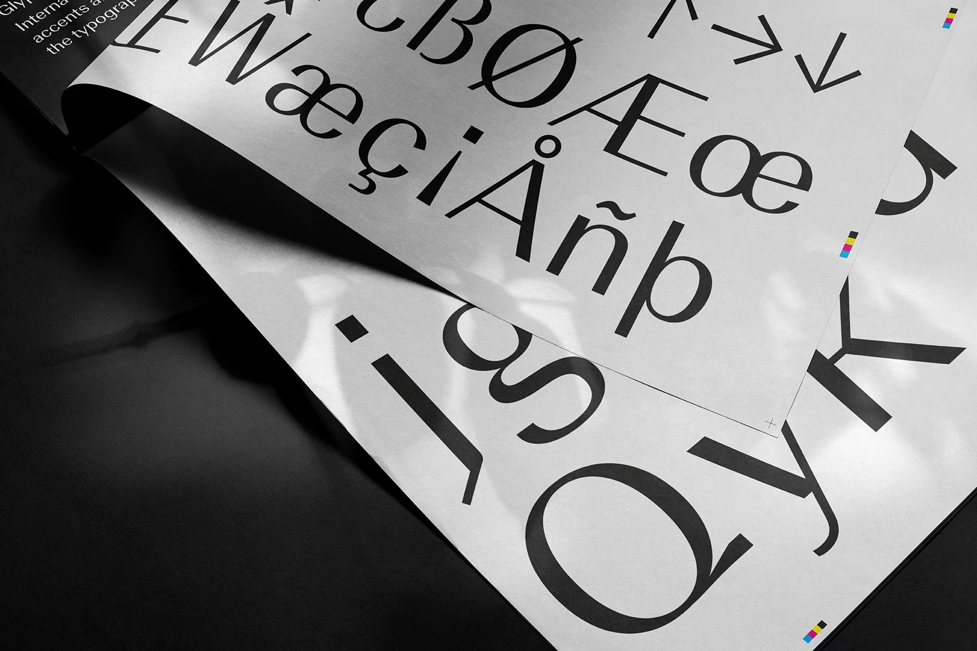 Sheets of paper display large, bold typography including glyphs and unique letterforms, set against a sleek, black background.