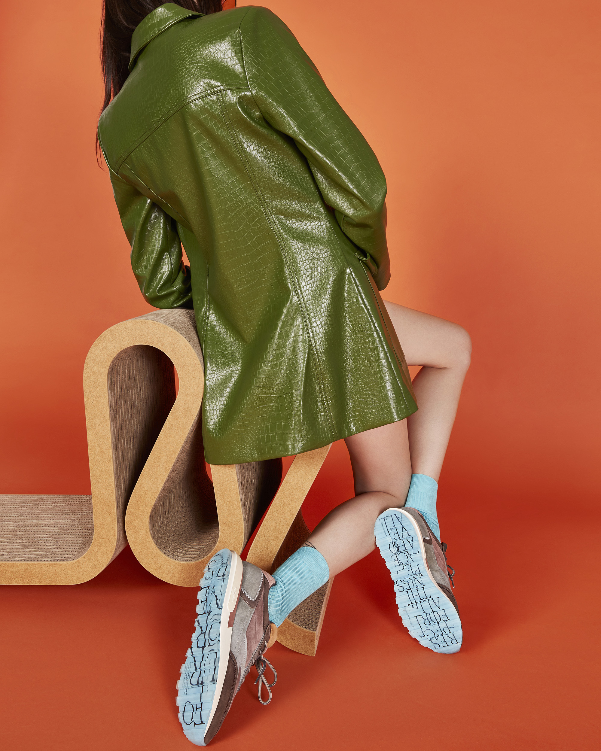 Back shot of a woman wearing a green faux crocodile skin coat and pastel blue socks with brown and baby blue platform sneakers.