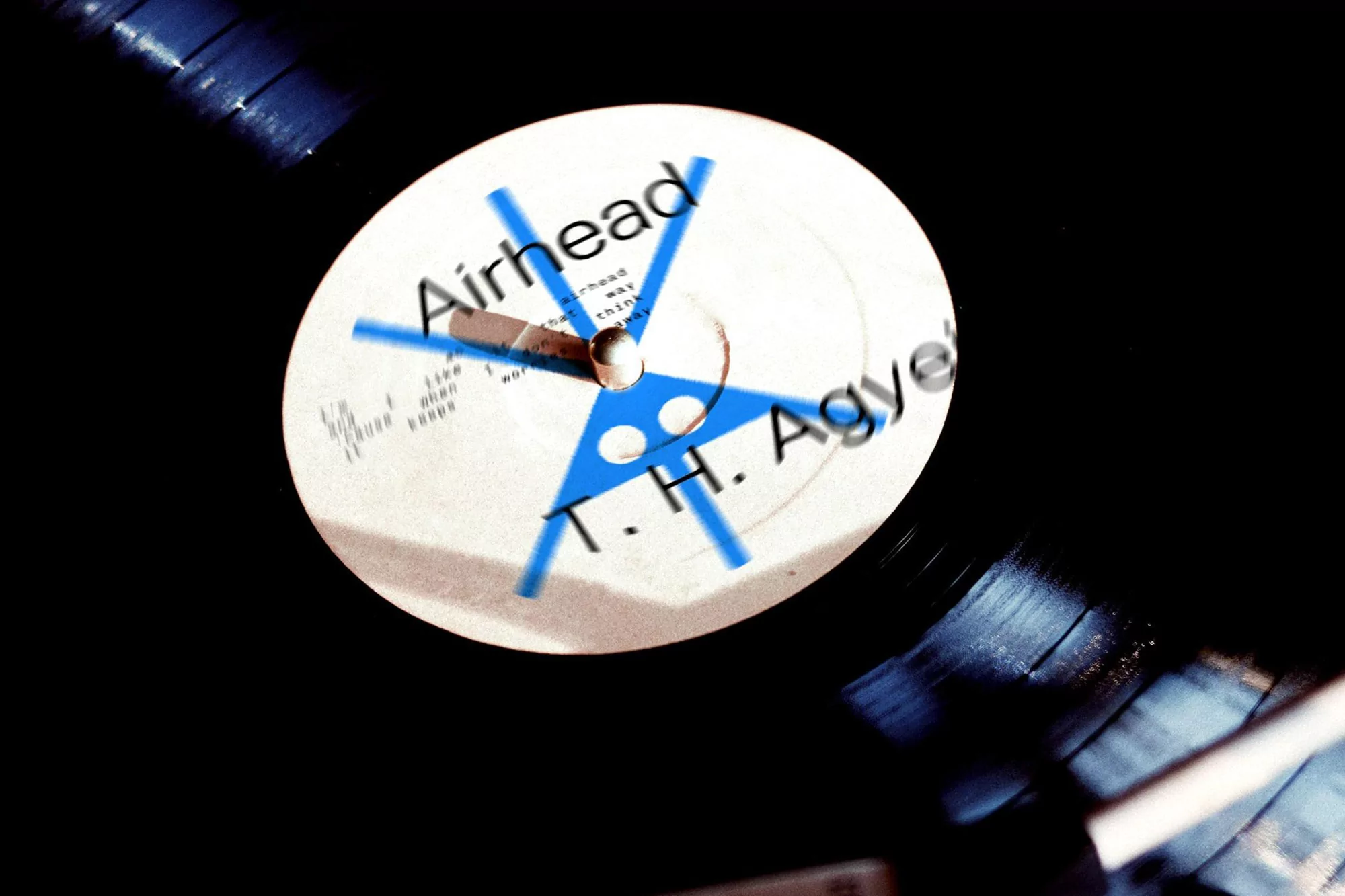 Macro photograph of a black vinyl record with a white label, featuring blue graphics and the words 'Airhead' and 'T.H. Agye'
