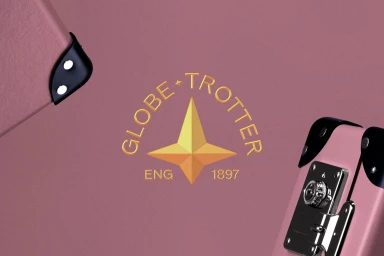 Globe-Trotter brand identity featuring a gold compass star logo on a pink suitcase with black leather corners and metal hardware.