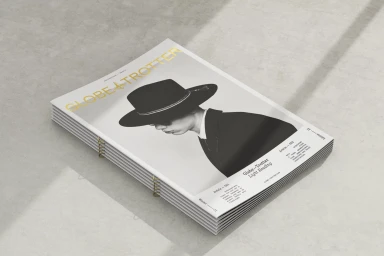 A stack of Globe-Trotter brand magazines featuring black and white cover photography and gold foil typography on a light concrete surface