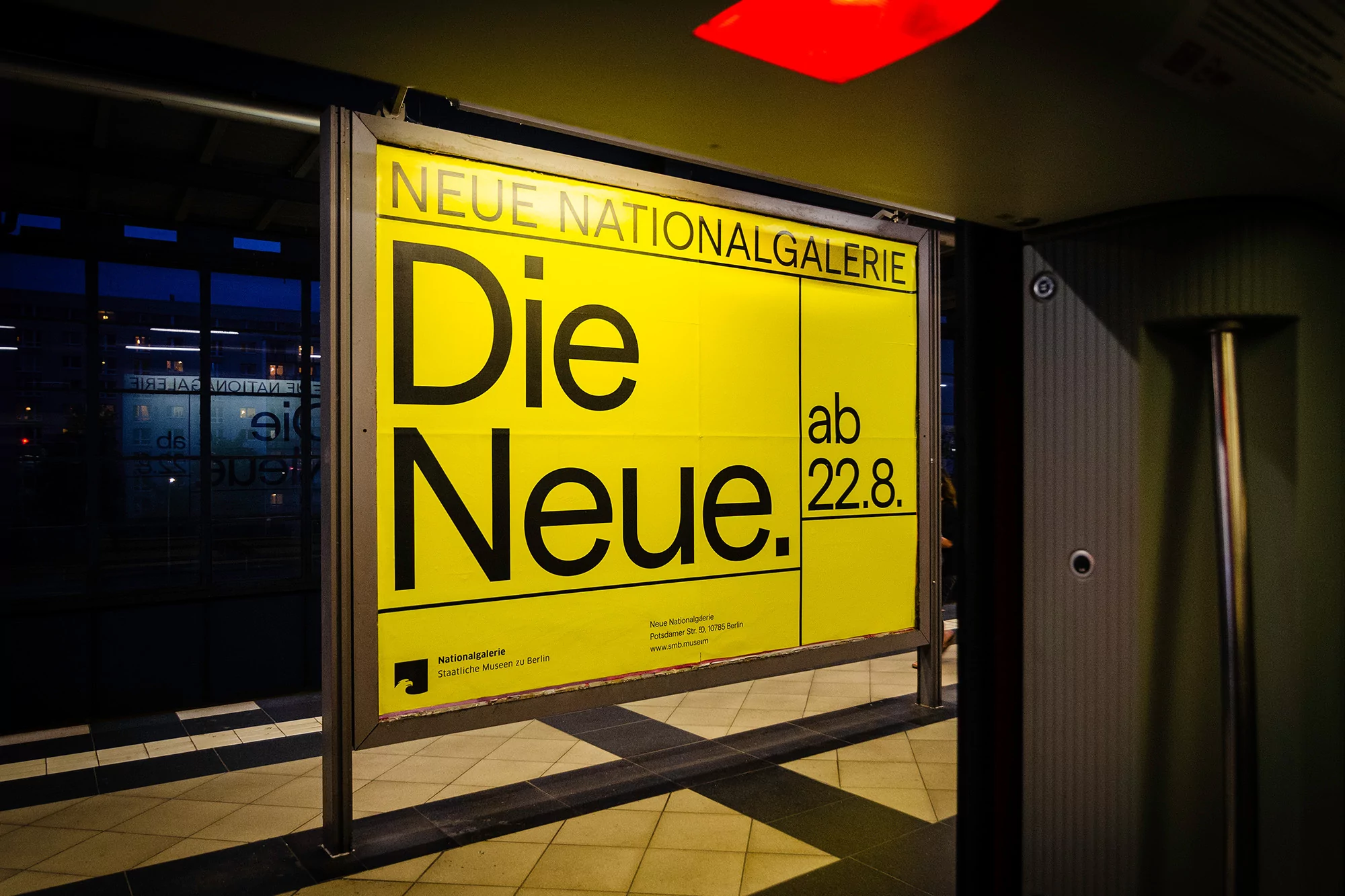 Outdoor advertising poster for Neue Nationalgalerie in Berlin featuring a bold yellow background and black text on a train platform.