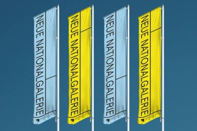 Four tall vertical flags featuring Neue Nationalgalerie typography against a clear blue sky