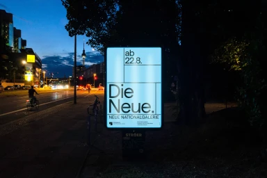 Illuminated advertising display on a city street at night showcasing brand identity graphics for Neue Nationalgalerie.