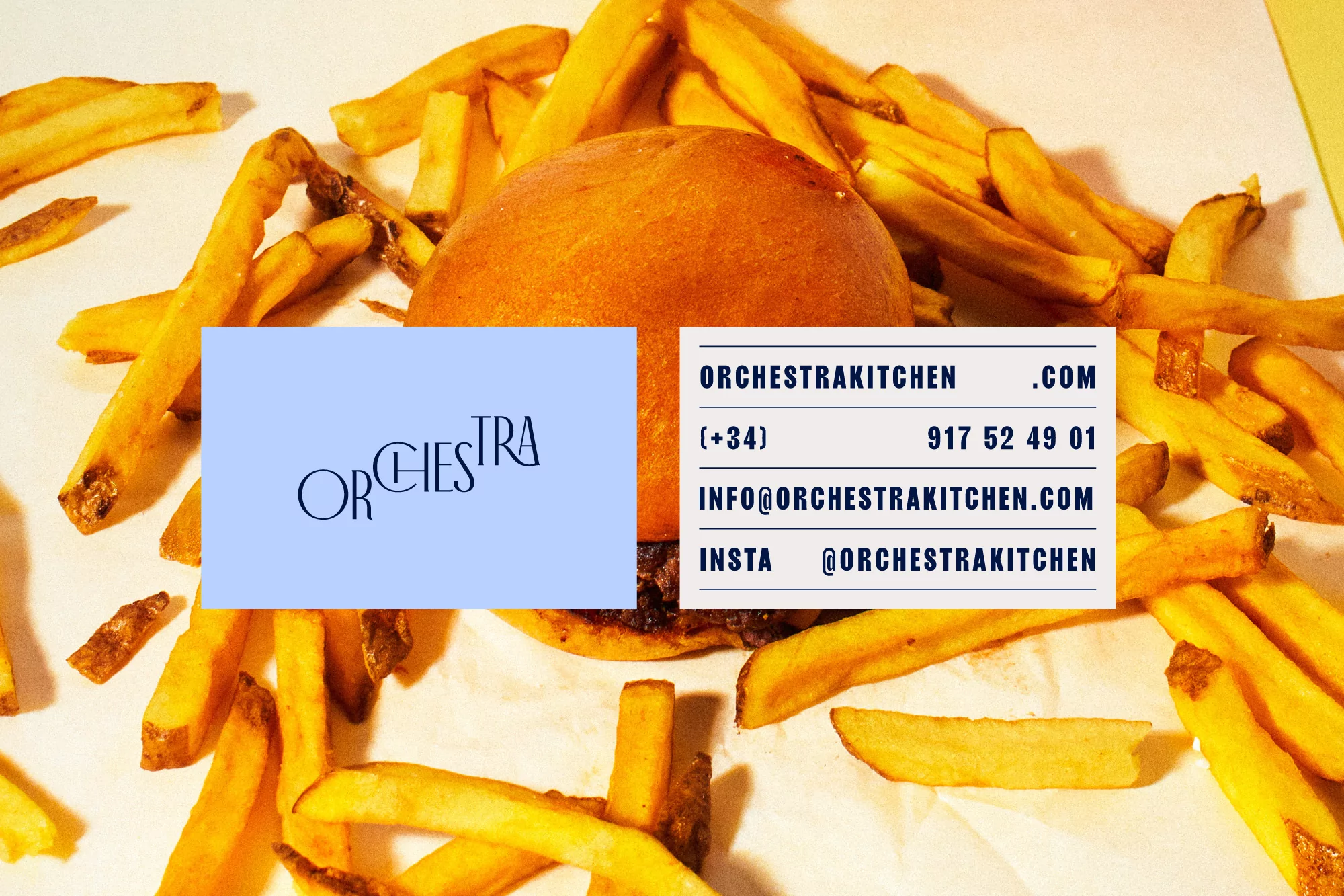 Overhead shot of a burger partially obscured by a business card, with french fries scattered around on a white paper surface.