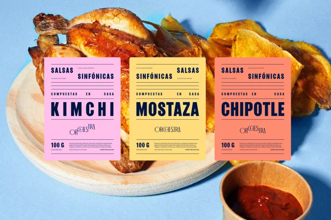 Overhead shot of a roasted chicken next to potato wedges and three sauce jars in pink, yellow, and orange on a blue background.