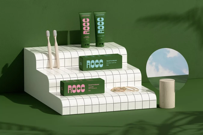 Product photography showcases green ROCC toothpaste tubes and boxes on a tiered white display with toothbrushes, against a green background.