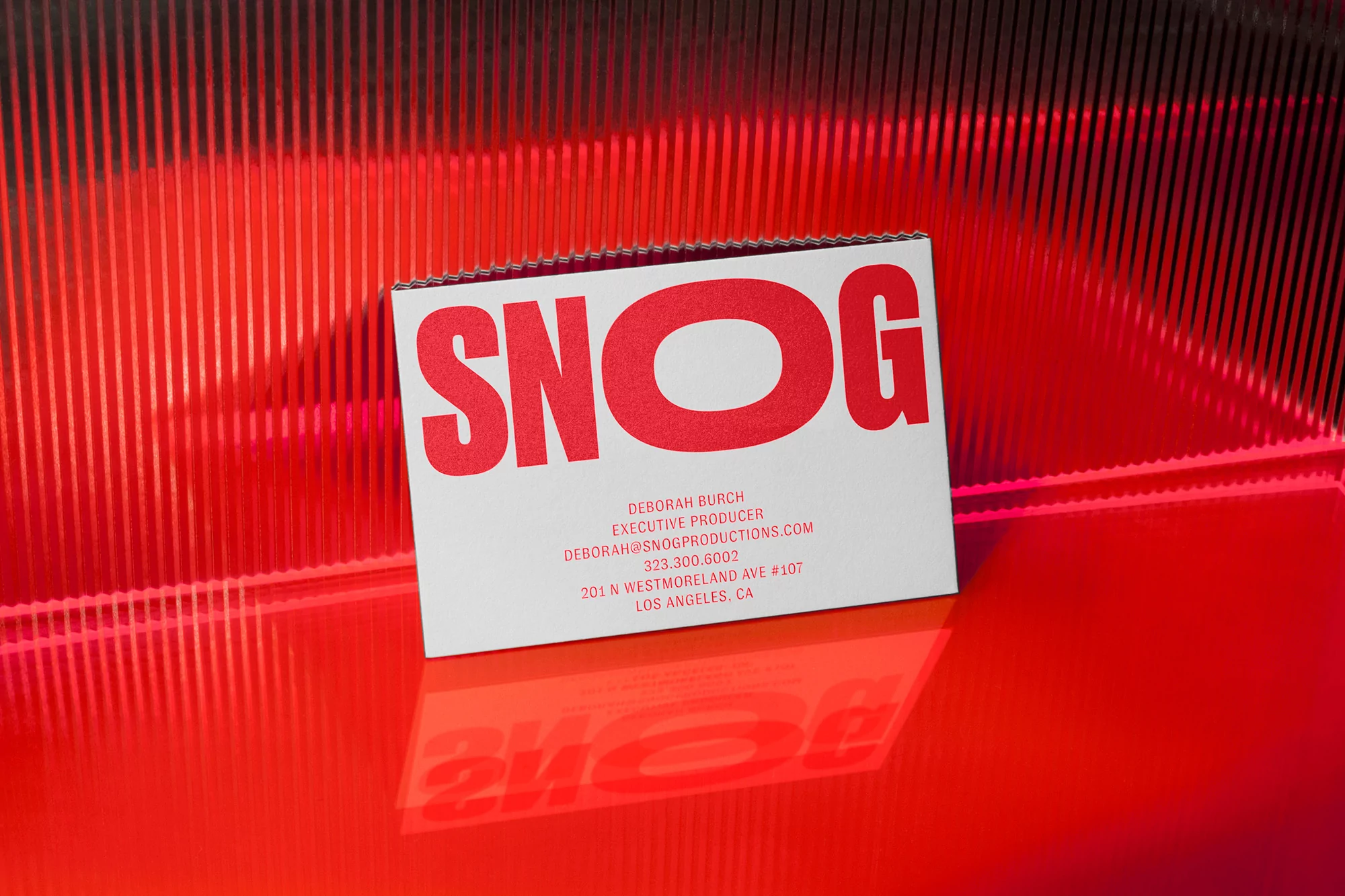 Close-up of a white business card with the name SNOG printed in red, set against a red and black striped background.
