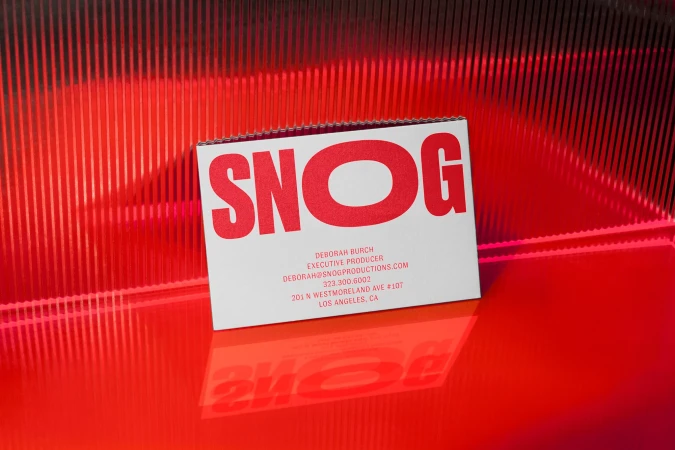 Close-up of a white business card with the name SNOG printed in red, set against a red and black striped background.