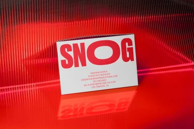 Snog Productions business card displaying red typography on a white card, set against a ribbed red surface with reflection.