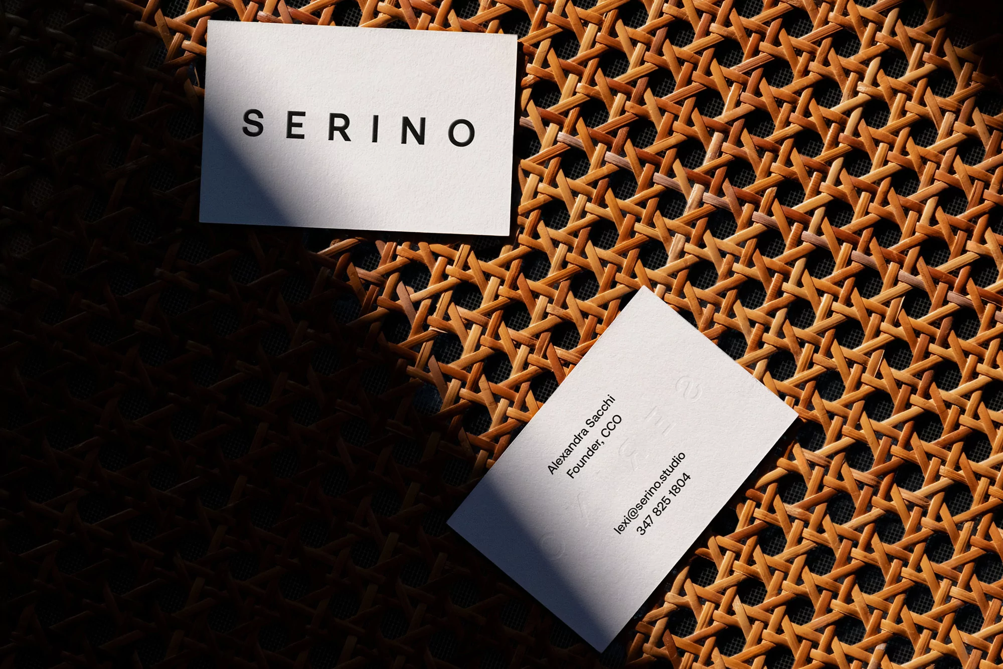 Two business cards with text on top of a woven surface, one with the company name and the other with contact information.