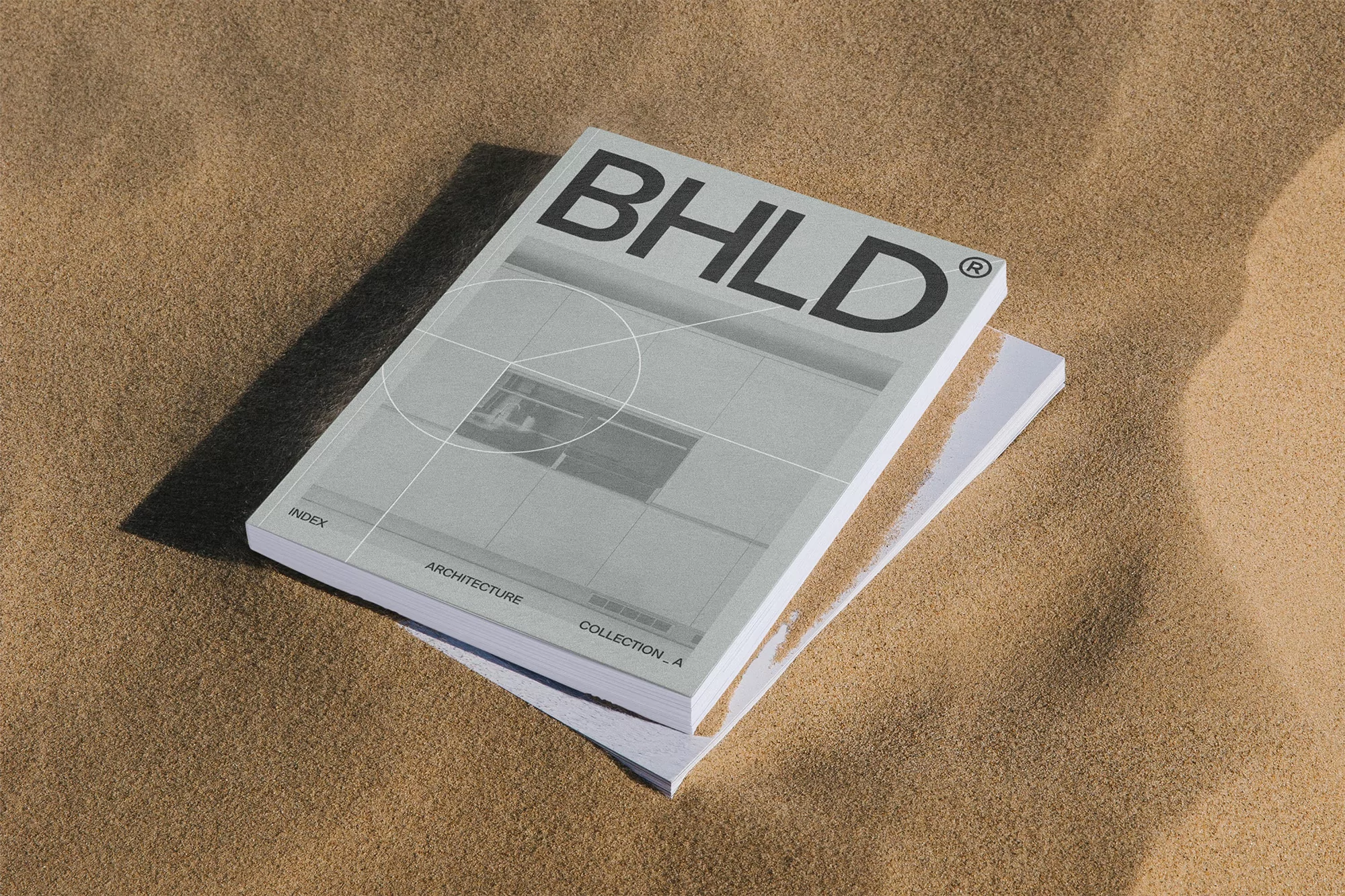 Architecture book titled BHLD on a pile of books on a sandy surface, showcasing a modern design and minimalist aesthetic.