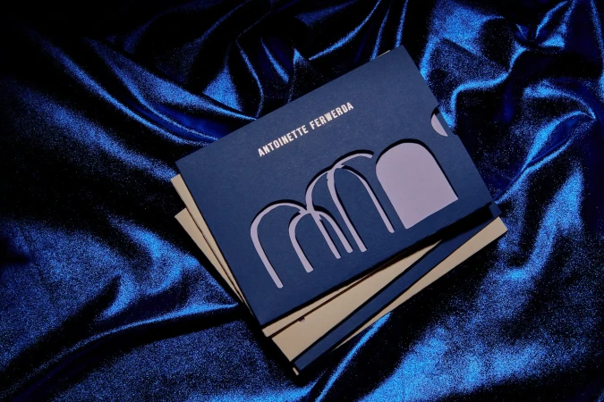 Stationery set with a dark blue business card featuring a unique geometric cut-out design, resting on a shimmering blue satin fabric backdrop.
