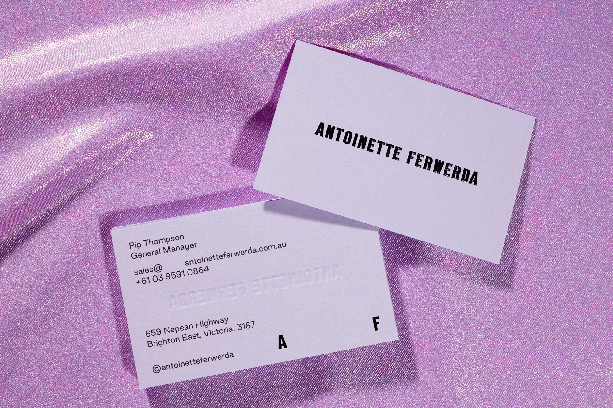 Two business cards with Antoinette Ferwerda branding on a shiny lilac textile background. Crisp, professional presentation.
