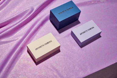 Three stacks of business cards in blue, purple, and cream on a shiny pink satin fabric background.
