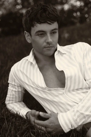 Portrait of a handsome adult male lying on green grass, wearing an unbuttoned striped shirt, photographed outdoors.