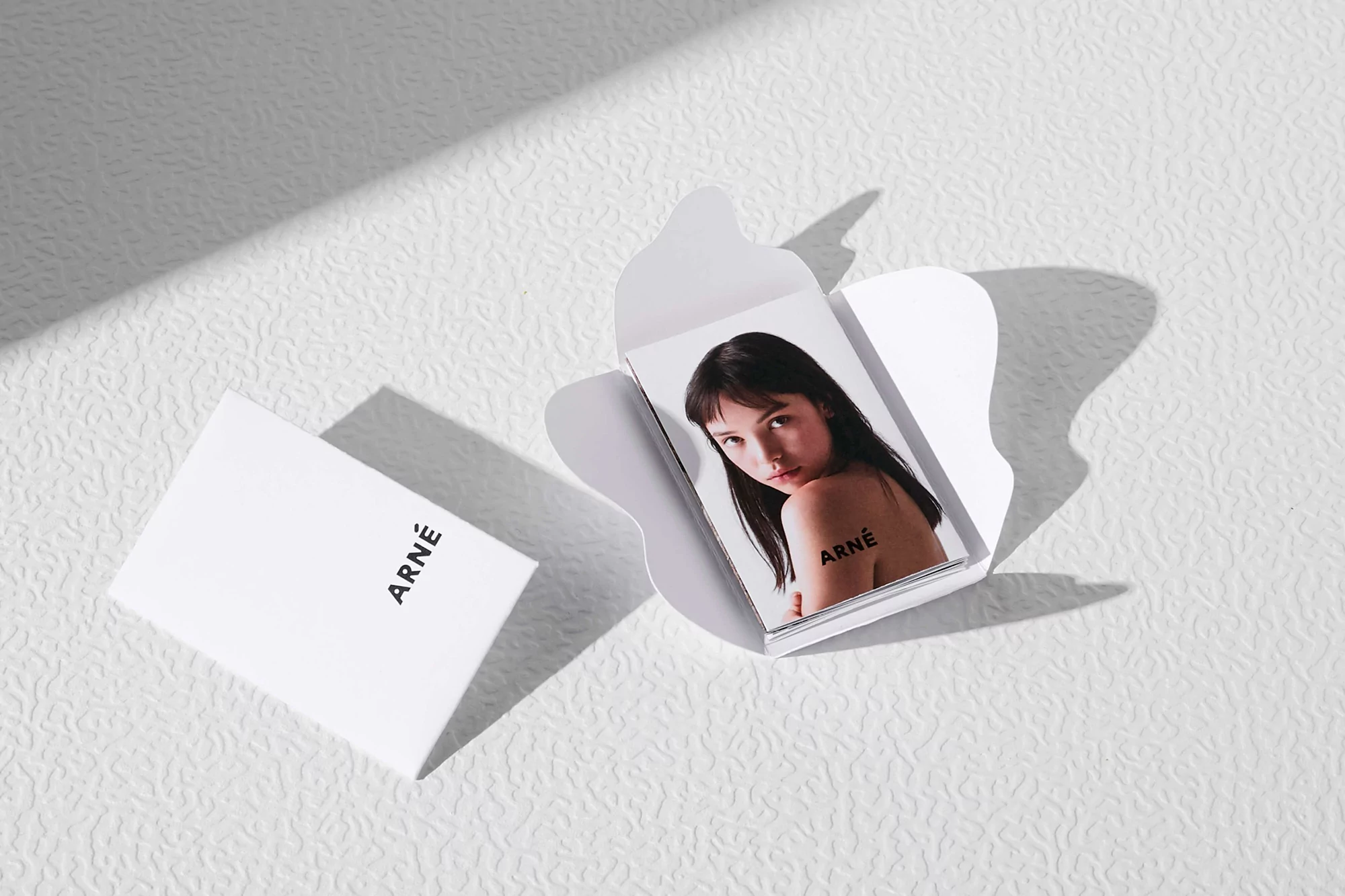 An open white package reveals a photo of an adult woman with black hair and a tattoo on her back. Another closed package sits beside it.