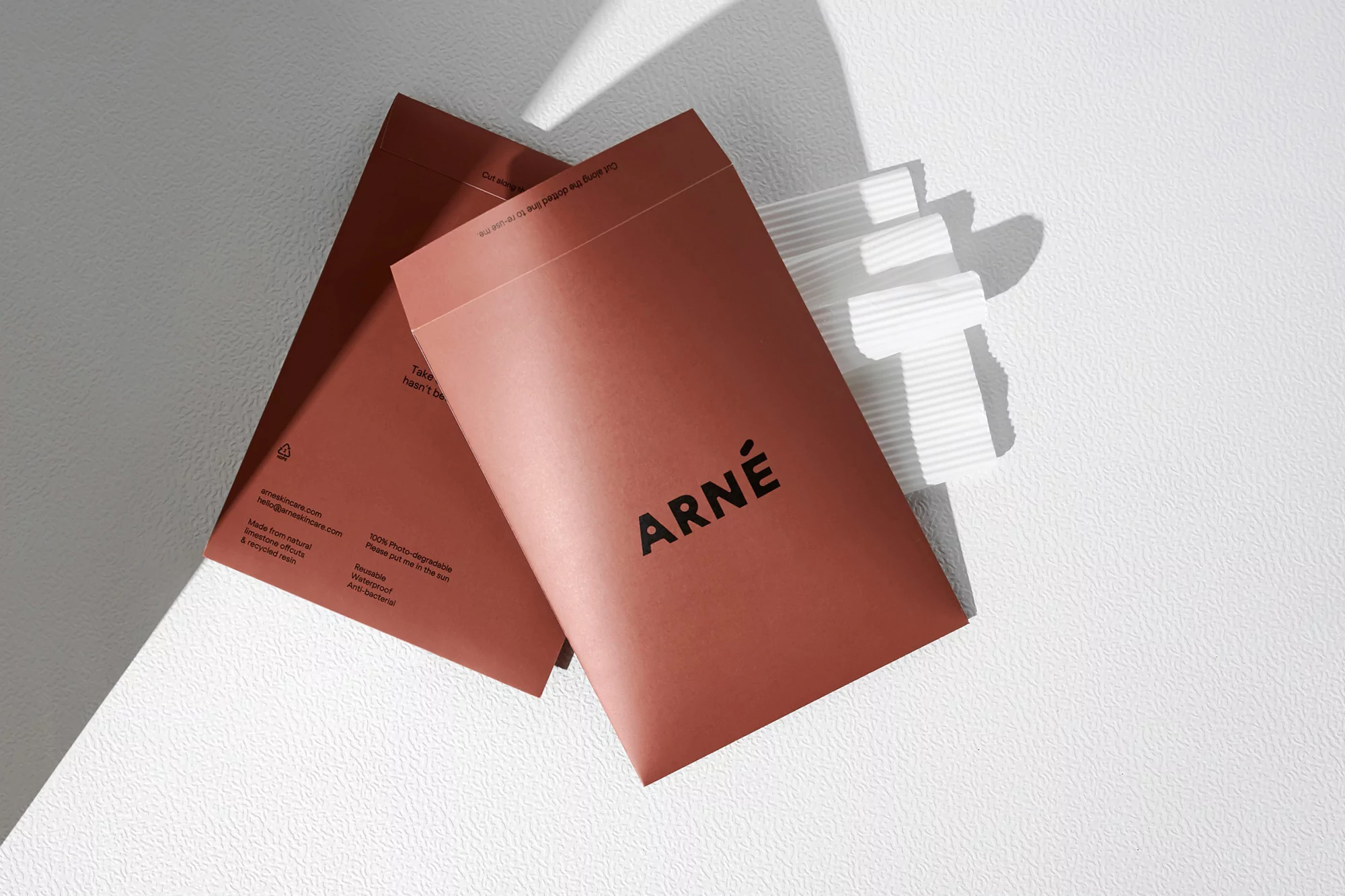 Two brown ARNE-branded envelopes with linear detail lay on a white surface in bright lighting, showcasing minimalist design and branding.