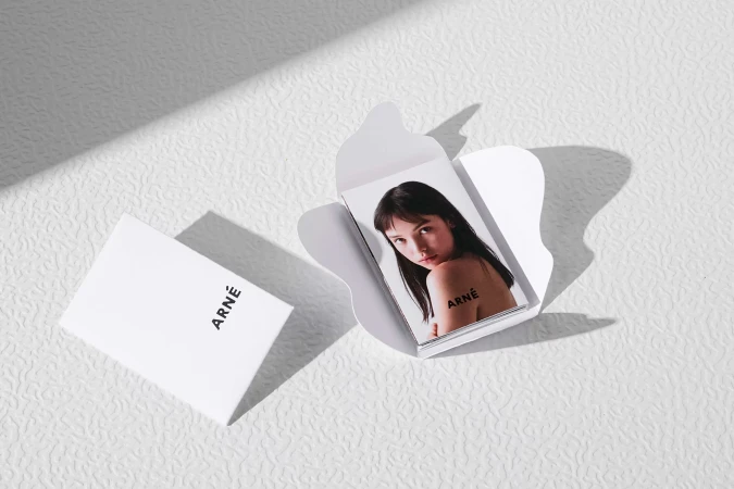 An open white paper packaging box containing printed cards with a portrait of a woman, set on a textured white surface.