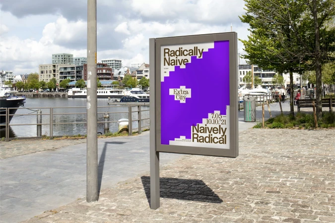 Outdoor advertising poster on a sidewalk featuring bold typography and a purple geometric design near a harbor on a cloudy day.