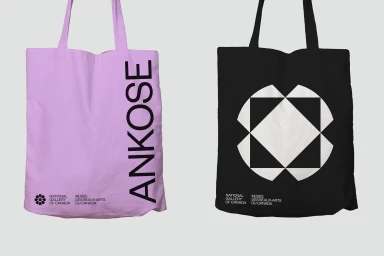 Two canvas tote bags displayed against a light grey background, one pink with vertical typography and one black with a geometric graphic.