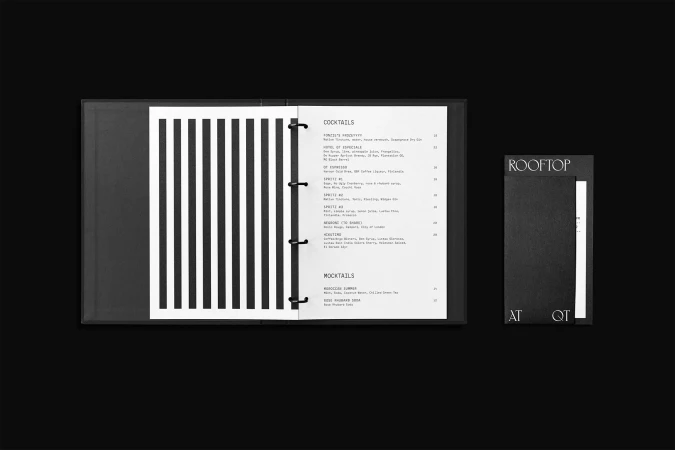 Open black menu on dark surface with bar and restaurant cocktail and mocktail list, alongside smaller menu with "Rooftop at QT" text.