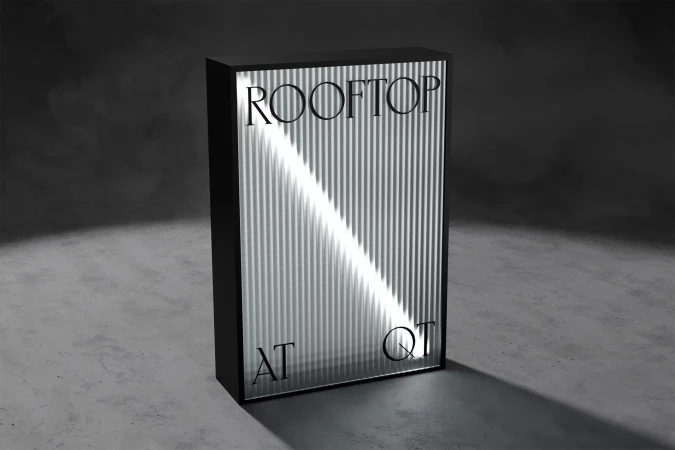 Vertical panel with black frame displays vertically-striped surface, illuminated by a diagonal beam, displaying 'Rooftop at QT' text.