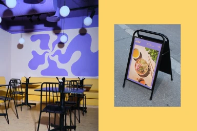 Restaurant interior with purple walls and yellow banquette seating alongside a sidewalk sign displaying food imagery