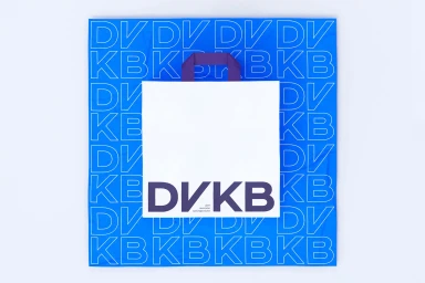 DVKB brand identity packaging featuring a white paper bag with purple typography centered on a blue patterned background