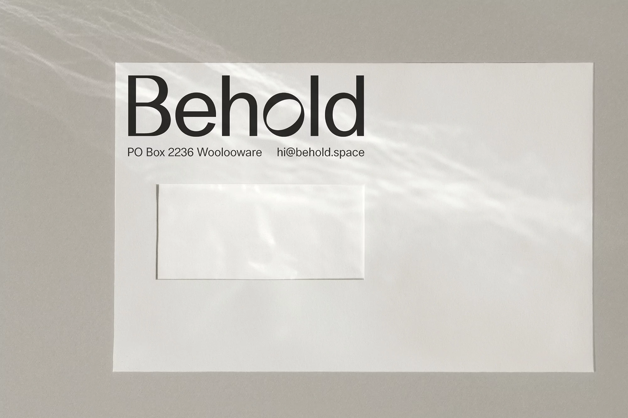 White envelope on grey surface with black company logo and address details, abstract light patterns on envelope surface.