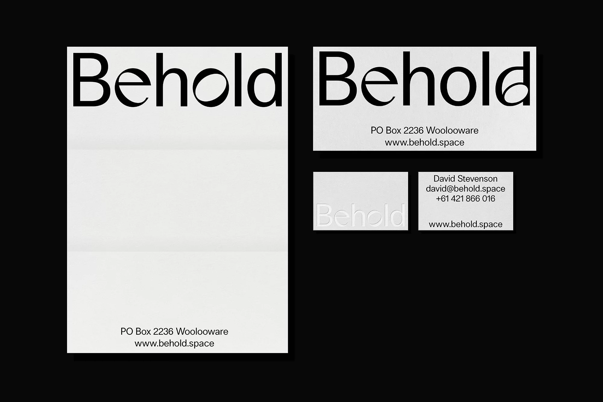 Close-up of four white paper materials with black text, neatly arranged on a black background displaying business card and stationery design.