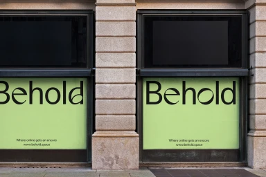 Storefront windows featuring the Behold brand identity with green panels and black typography