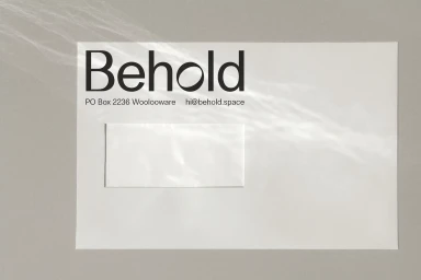 White envelope with the Behold brand logo displayed on a grey textured background with subtle light patterns