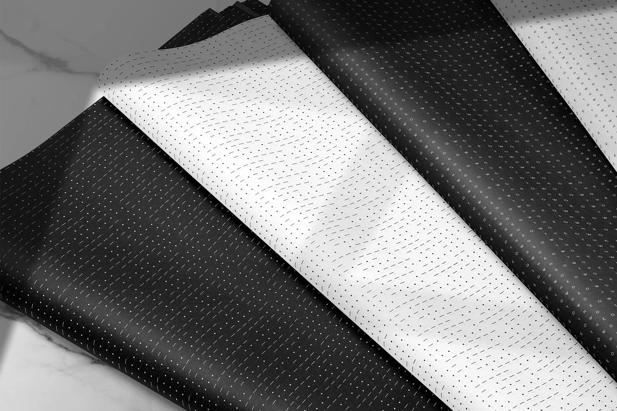 Overlapping sheets of patterned paper in black and white create an abstract design with minimalist dots and dashes. Neutral marble surface.